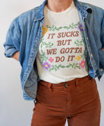 Person wearing a white t-shirt with colorful text and floral designs, paired with a denim jacket and brown pants.