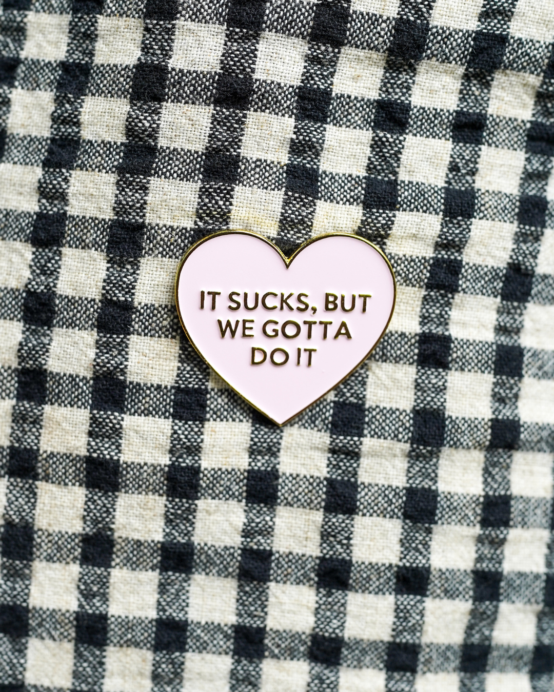 Heart-shaped enamel pin with text on a checkered fabric background