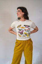 Person wearing a white t-shirt with butterfly designs and yellow pants against a plain background