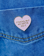 Heart-shaped enamel pin with motivational quote on blue denim background