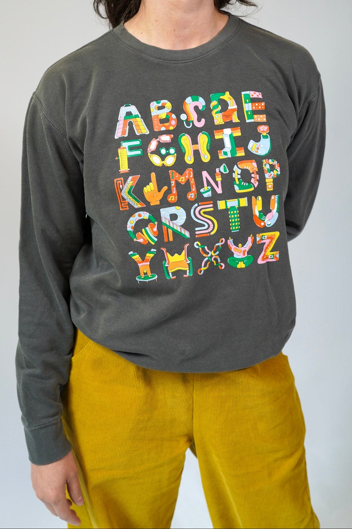 Person wearing a dark gray long-sleeve shirt with colorful alphabet design on a plain background