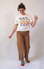 Person wearing a white t-shirt with colorful fish design and brown pants on a white background