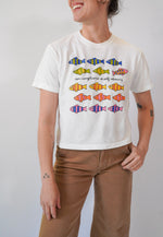 Person wearing a white t-shirt with colorful fish designs on a plain background