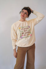 Person wearing a cream sweatshirt with floral text design on a plain background