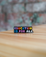 Colorful 'Education is for All' pin on a wooden surface with a blurred background