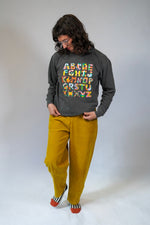 Person wearing a dark gray sweatshirt with colorful text and mustard yellow pants on a white background