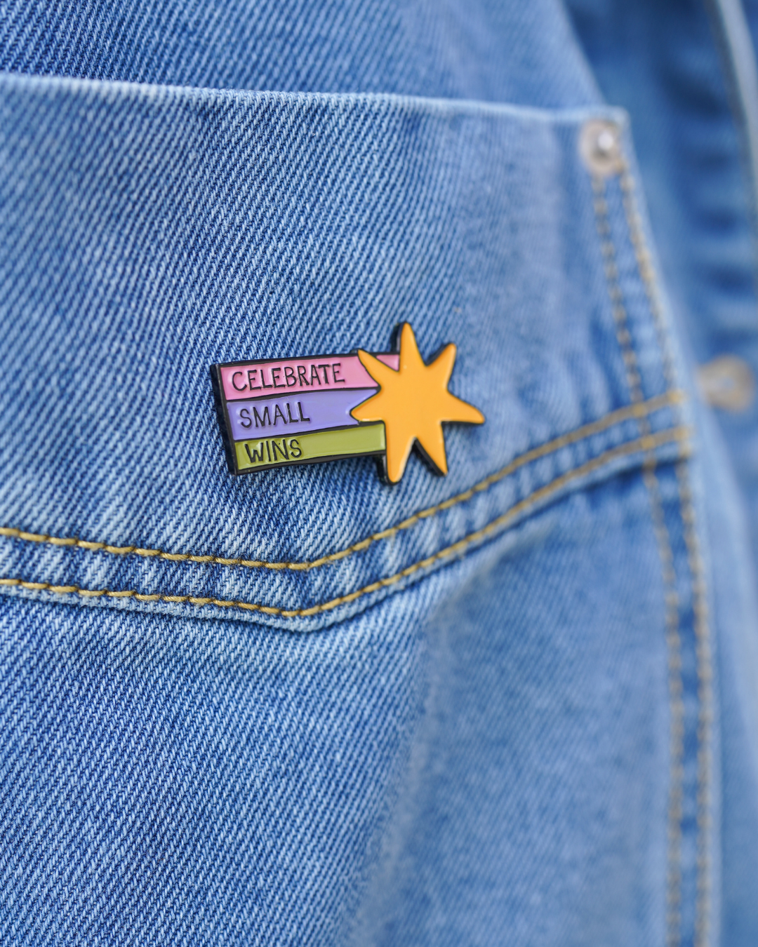 Pin with 'Celebrate Small Wins' text on a denim jacket