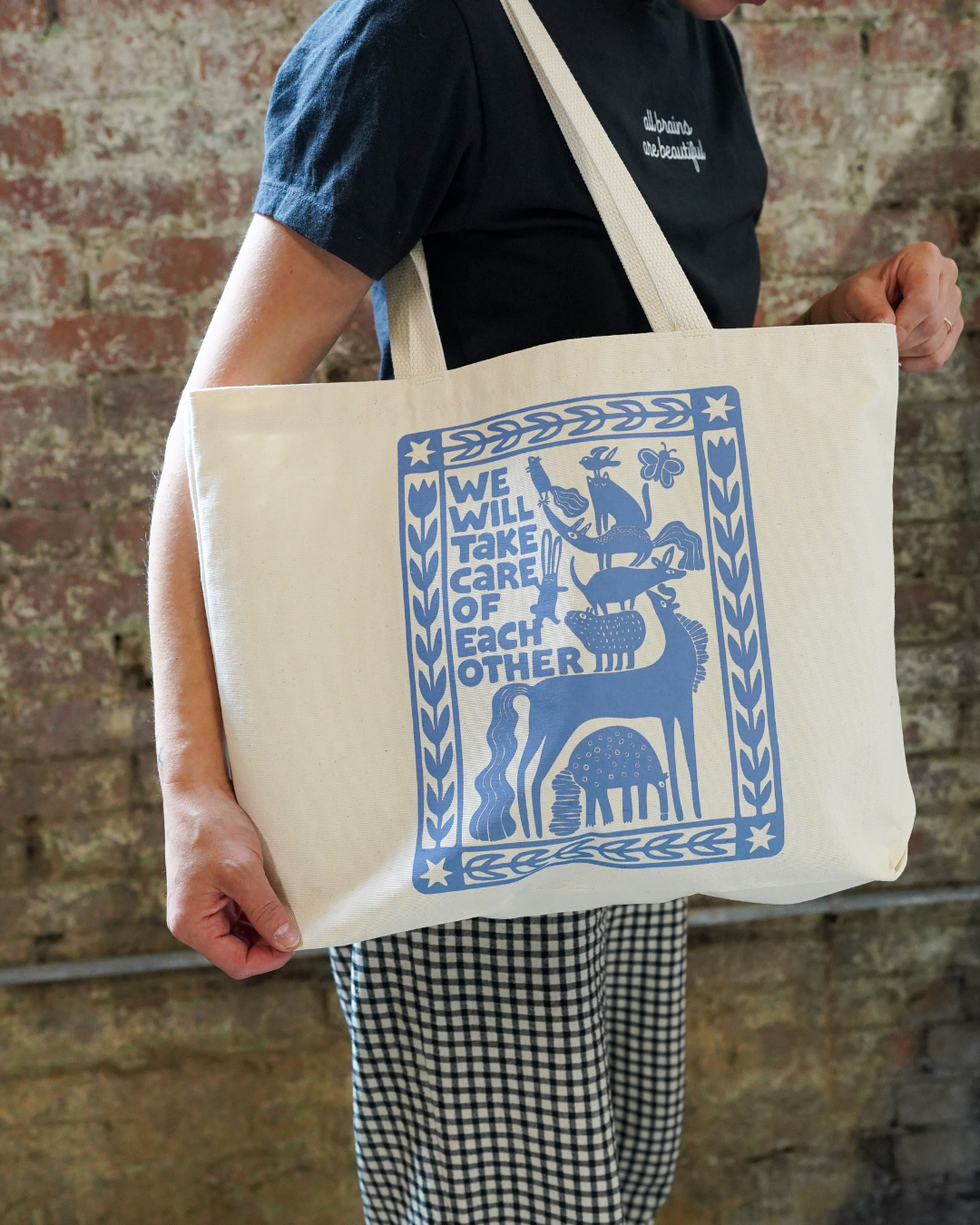 Person holding a tote bag with blue graphic design against a brick wall.