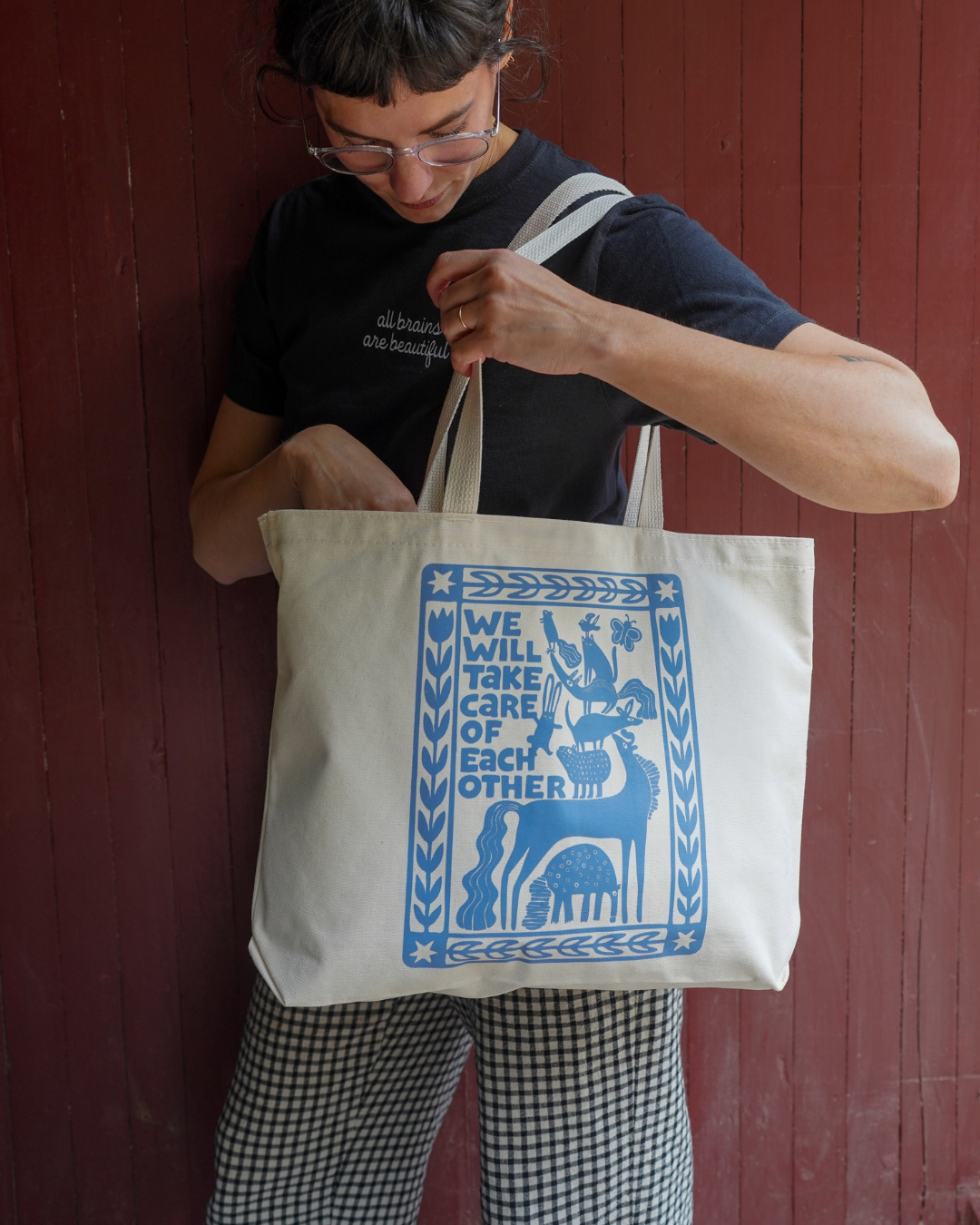 Person holding a tote bag with a blue design and text against a red wooden wall.