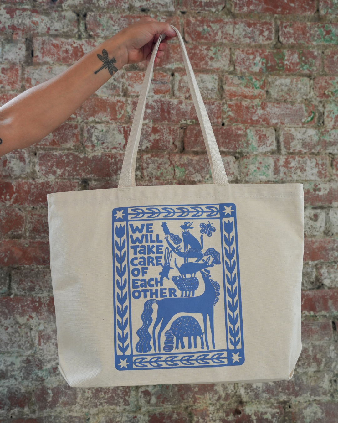 Tote bag with blue design and text held by a person against a brick wall.