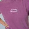 Person wearing a purple t-shirt with 'all brains are beautiful' text on a plain background
