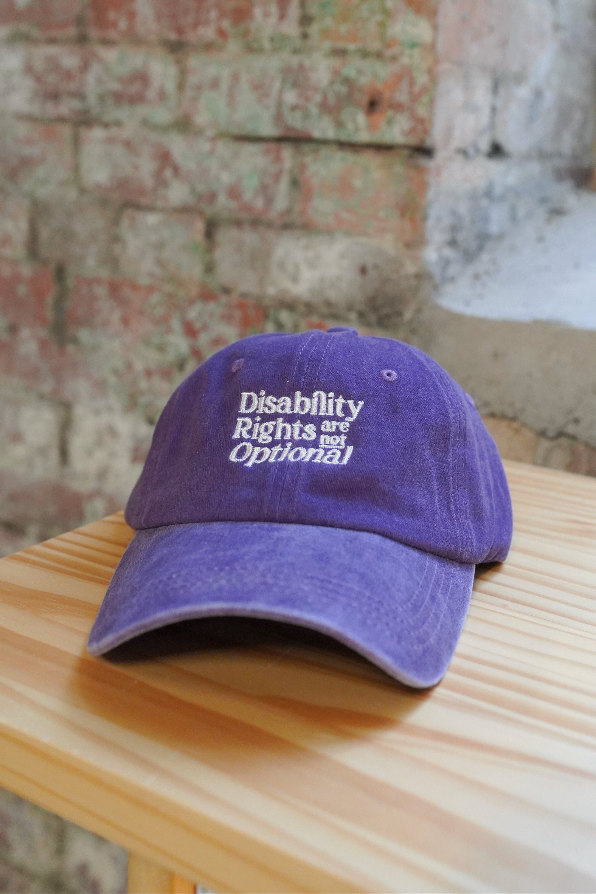Purple cap with text on a wooden surface with a brick wall background