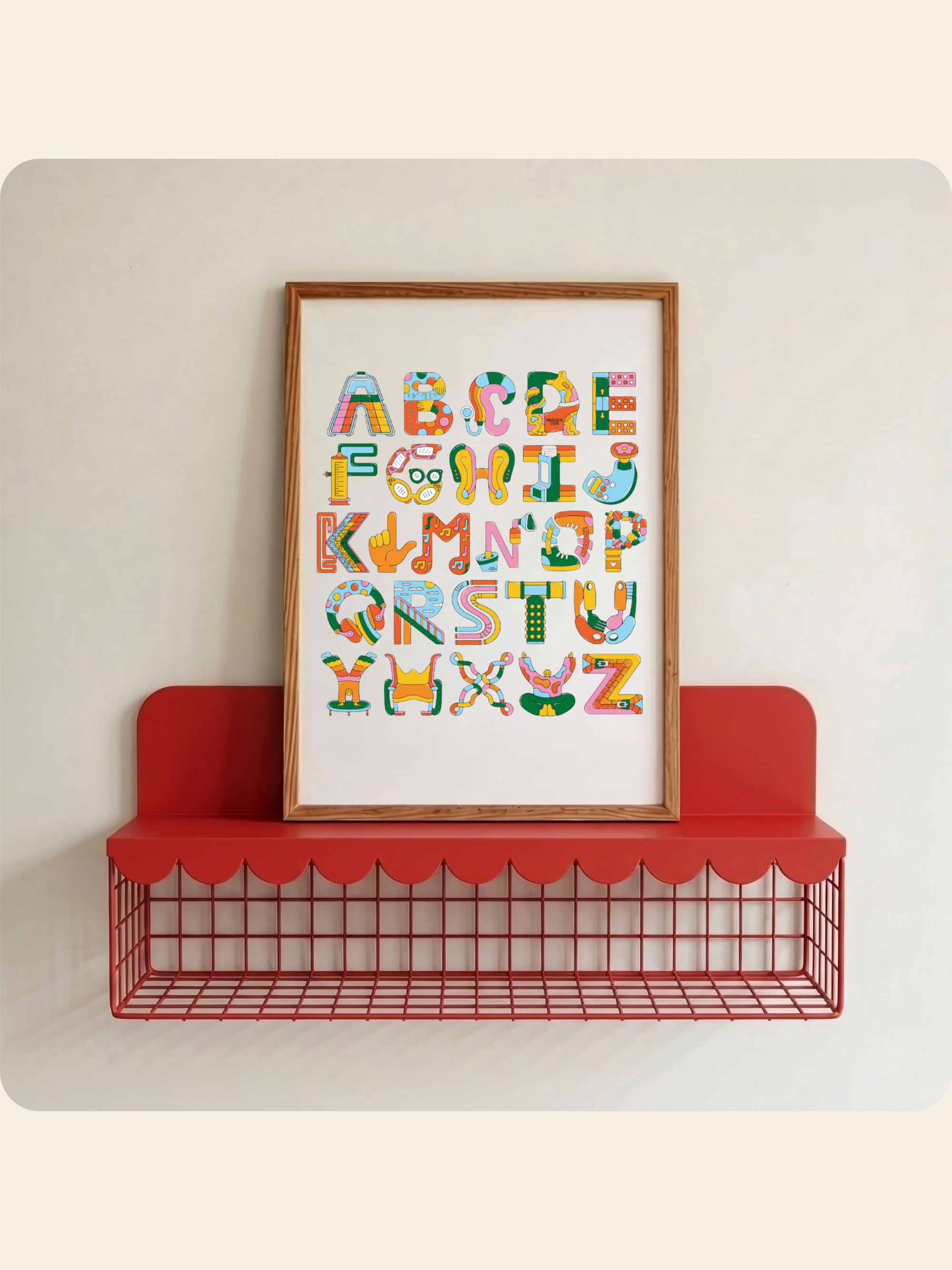 A framed alphabet art print featuring colorful letters with accessibility element illustrations, displayed on a red wire shelf against a light beige wall.