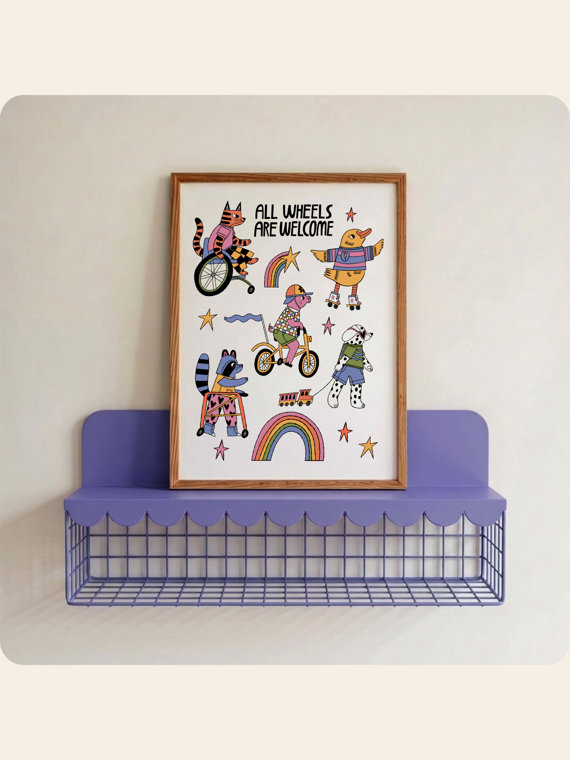 A framed whimsical art print with the text 'ALL WHEELS ARE WELCOME' and cartoon animals riding bicycles, displayed on a purple wire shelf against a light beige wall.