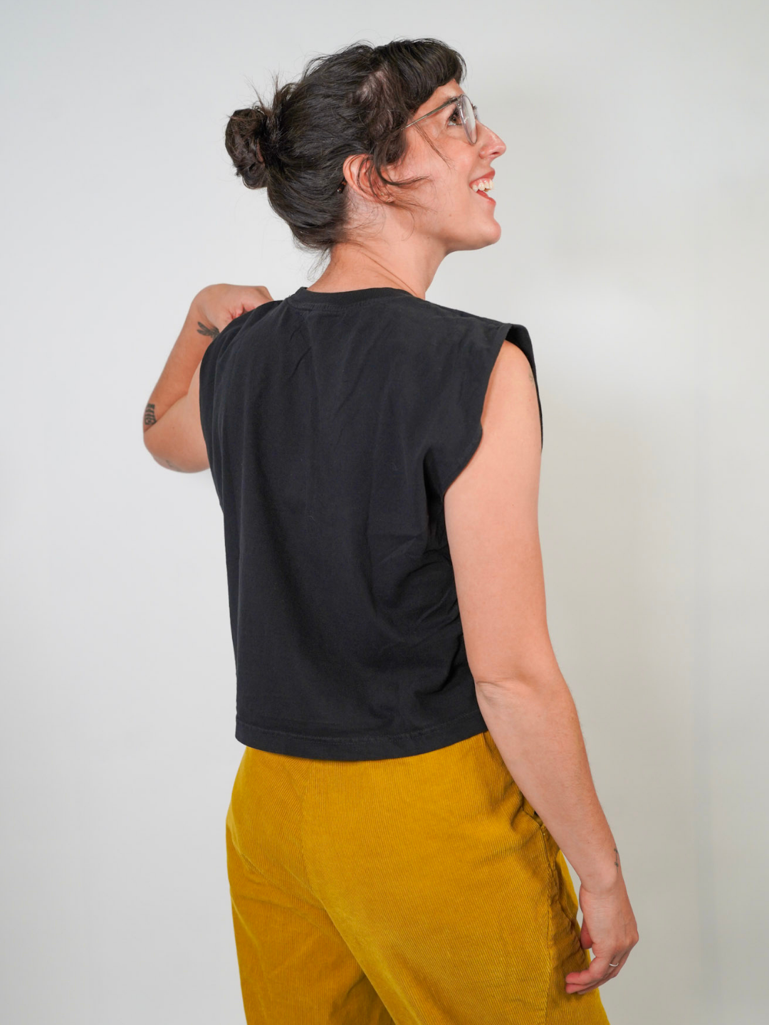 Woman wearing a black sleeveless top and mustard yellow pants against a plain background