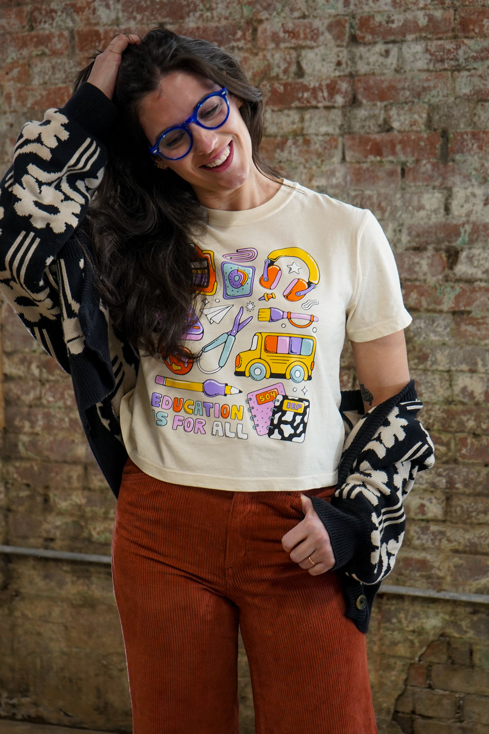 Person wearing a graphic t-shirt with colorful design, and red pants against a brick wall. 