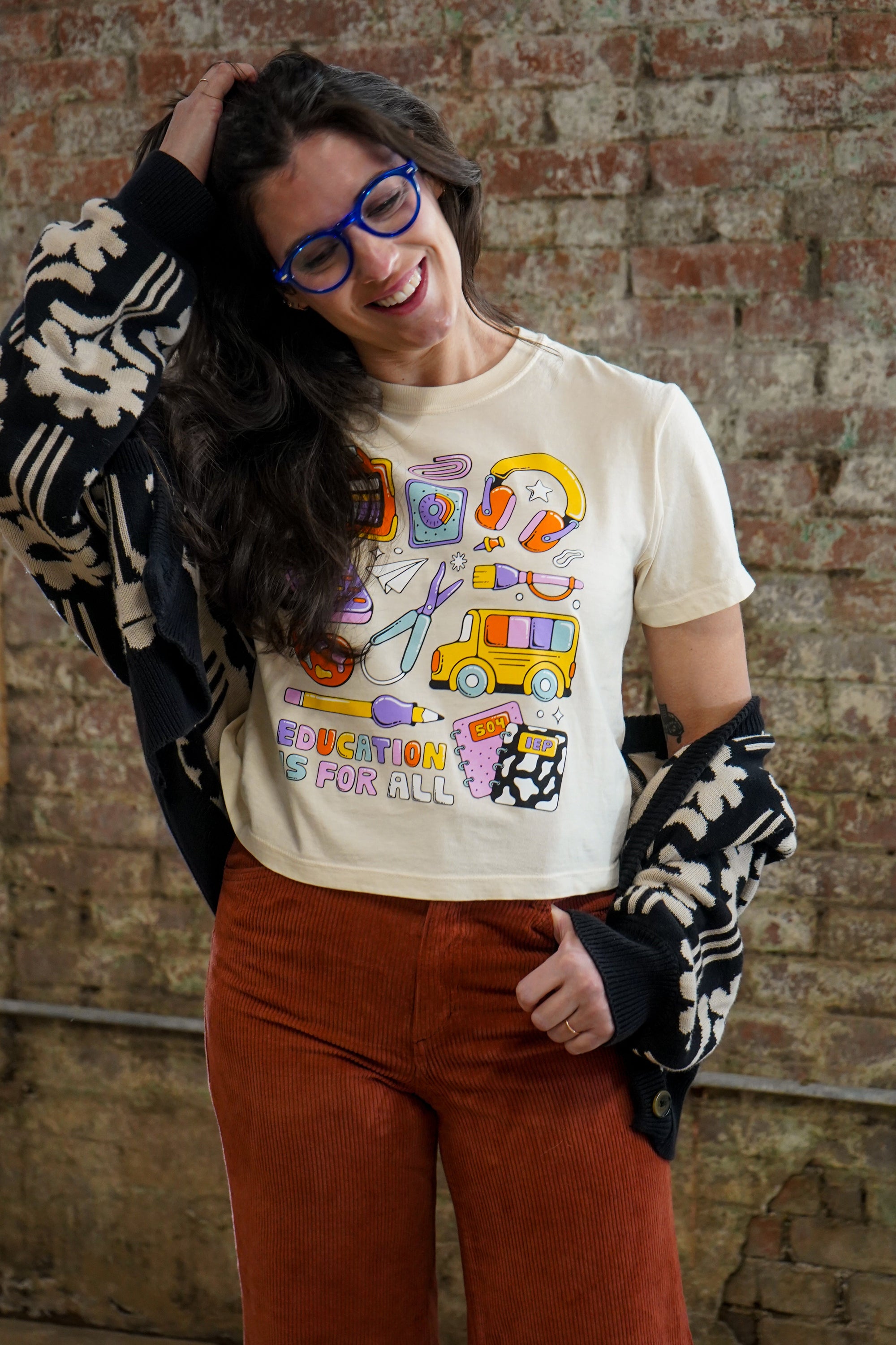 Person wearing a graphic t-shirt with colorful design, and red pants against a brick wall. 