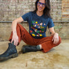 Person wearing a blue t-shirt with colorful design and red pants, sitting on a brick floor.