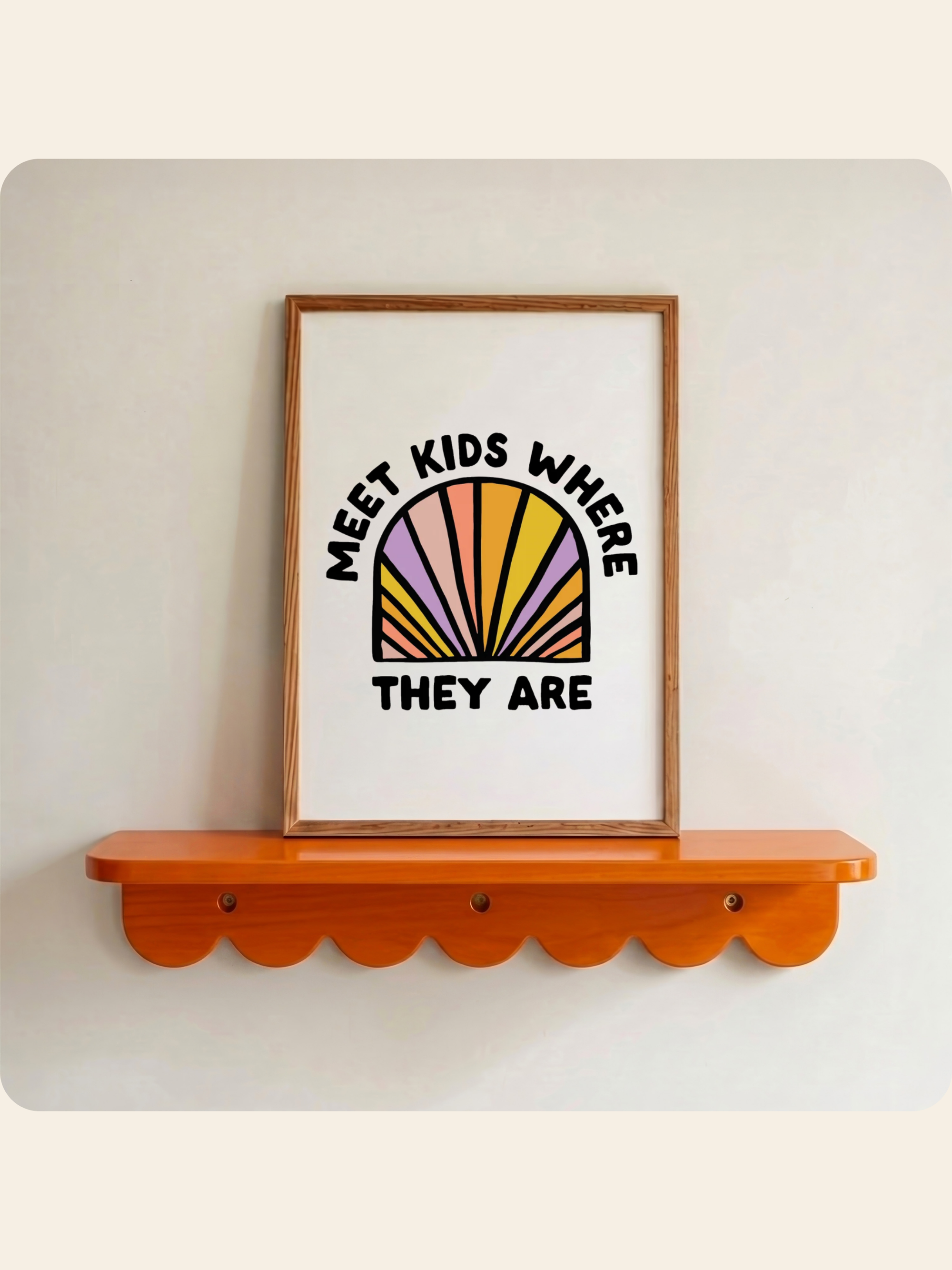 A framed wall art print with the text 'MEET KIDS WHERE THEY ARE' and a colorful sunburst graphic, displayed on an orange scalloped shelf against a light wall.