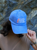 A person wearing a light blue baseball cap with an embroidered rainbow and the words 'Disability Rights are Optional' in white, shown against a rocky outdoor background.