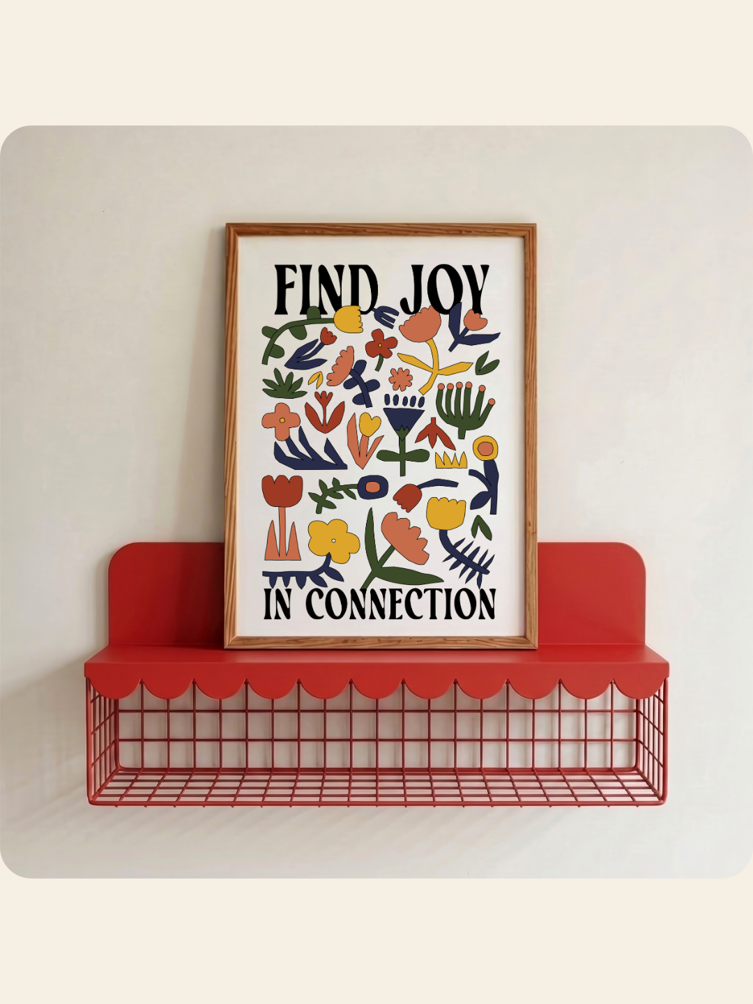 A framed art print with the text 'FIND JOY IN CONNECTION' and colorful floral illustrations, leaning on a red wire shelf against a light wall.