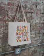 Tote bag with colorful alphabet letters hanging on a brick wall.