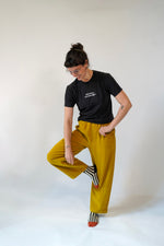 Person wearing a black t-shirt and mustard yellow pants on a white background