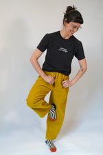 Person wearing a black t-shirt and mustard yellow pants on a white background