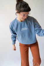 Person wearing a blue sweatshirt with text and brown pants on a plain background