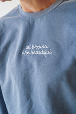 Blue sweatshirt with 'all brains are beautiful' text on a plain background