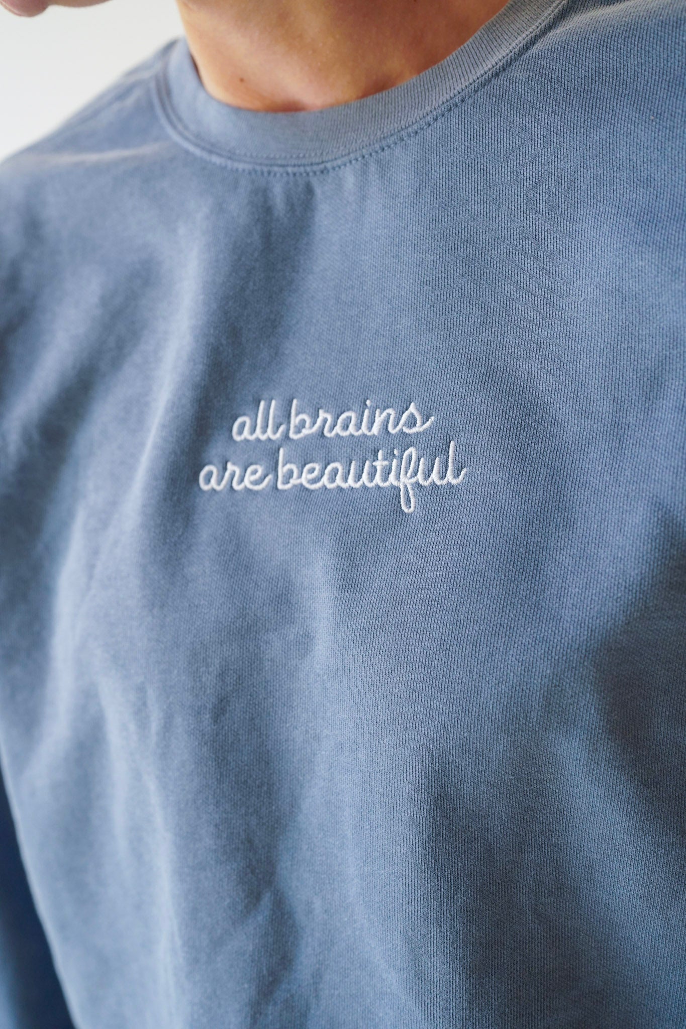 Blue sweatshirt with 'all brains are beautiful' text on a plain background