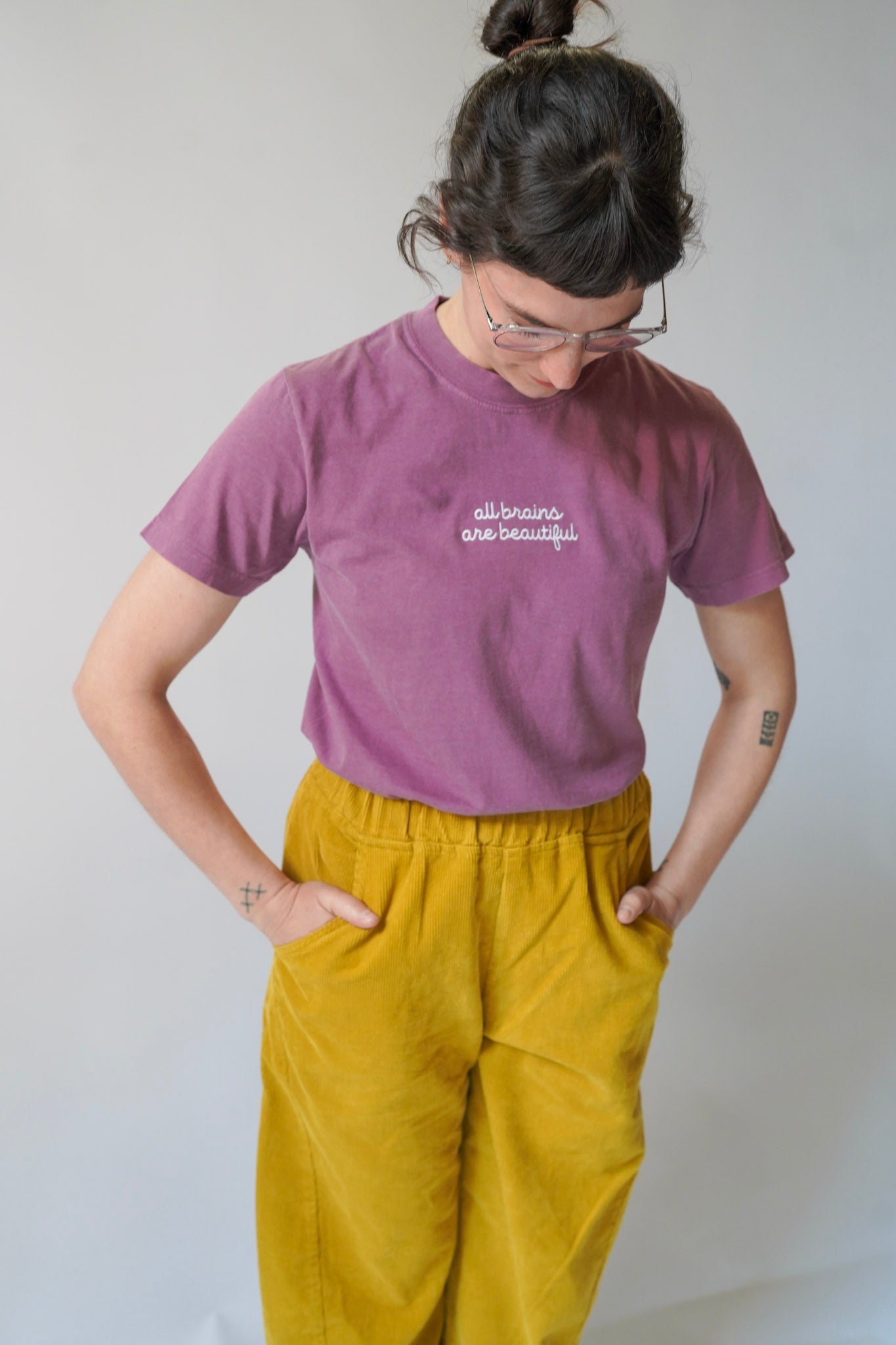 Person wearing a purple t-shirt with text and yellow pants against a plain background