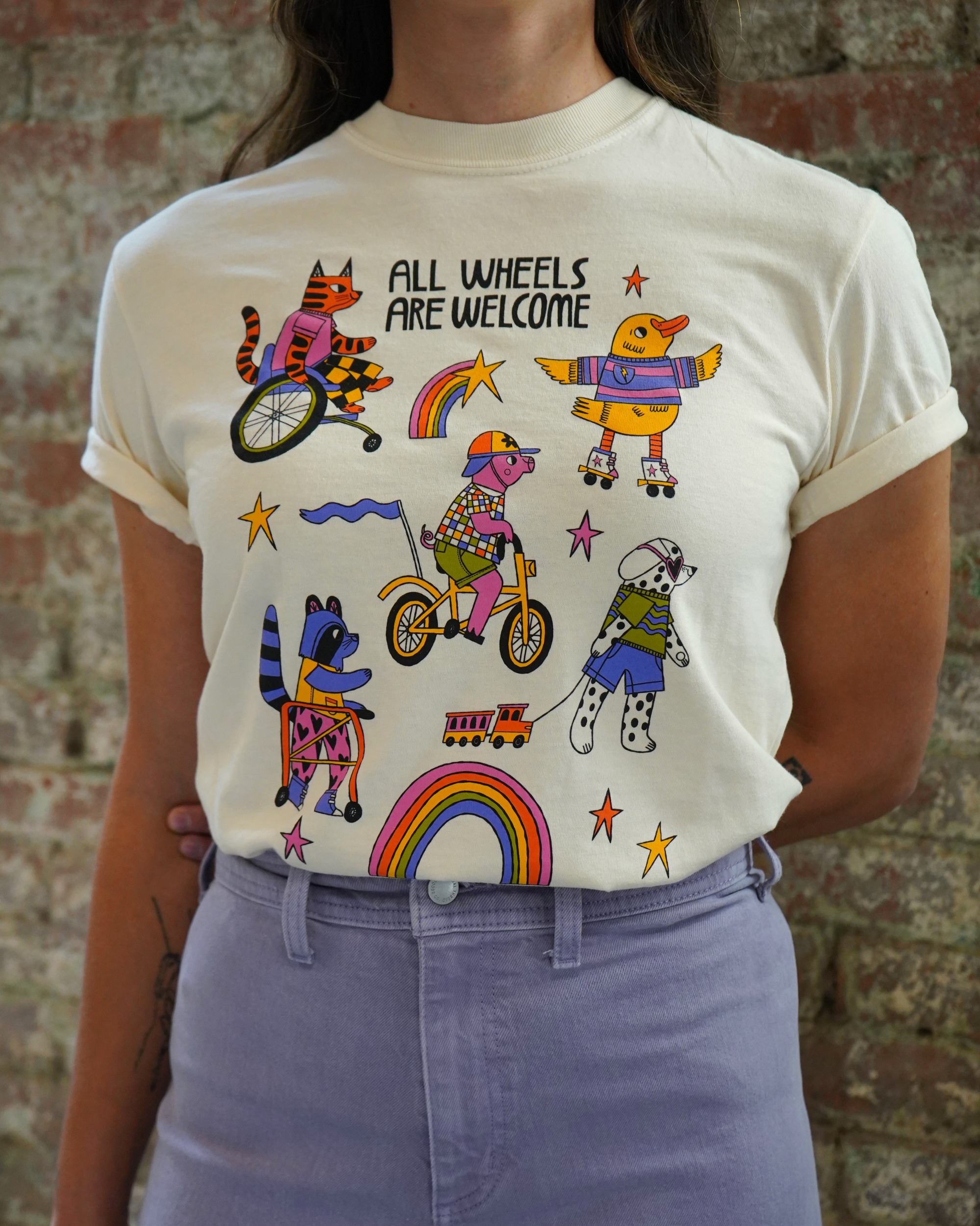 Person wearing a t-shirt with colorful illustrations and text against a brick wall.