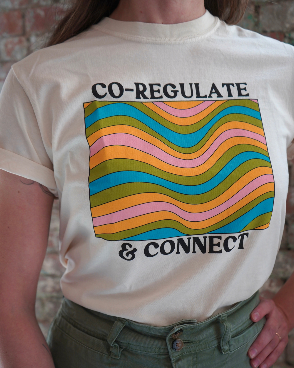 A person wearing a beige t-shirt with the text 'CO-REGULATE & CONNECT' and colorful abstract shapes.