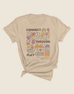 A beige colored t-shirt with a graphic design that includes various playful icons and the text 'CONNECT THROUGH PLAY'.