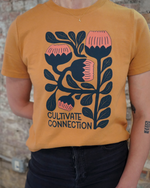 Person wearing a mustard yellow t-shirt with floral design and 'Cultivate Connection' text.