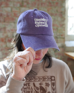 Person wearing a purple cap with 'Disability Rights are Not Optional' text, blurred background