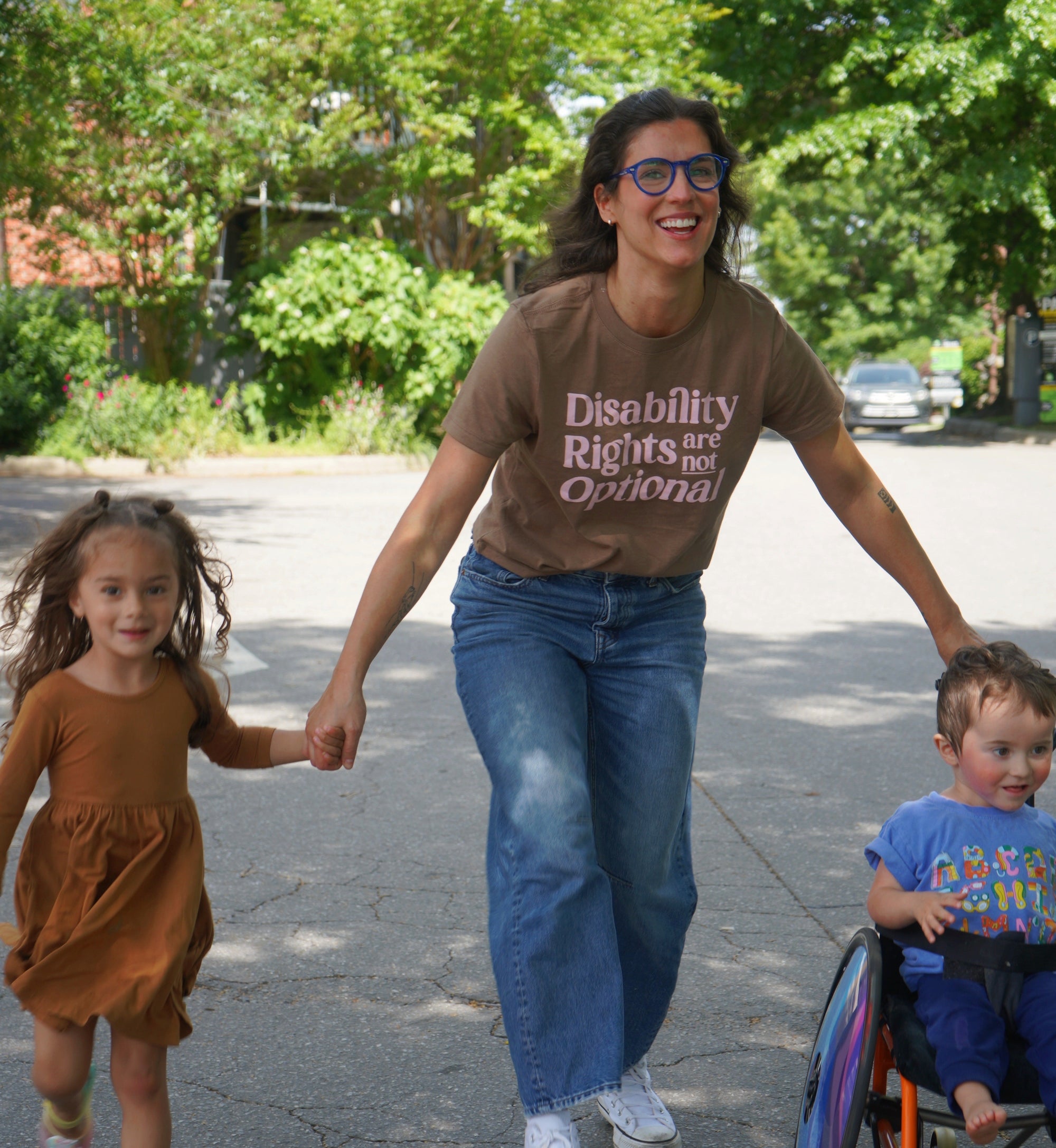 Woman walking with two children, one in a wheelchair, on a street.