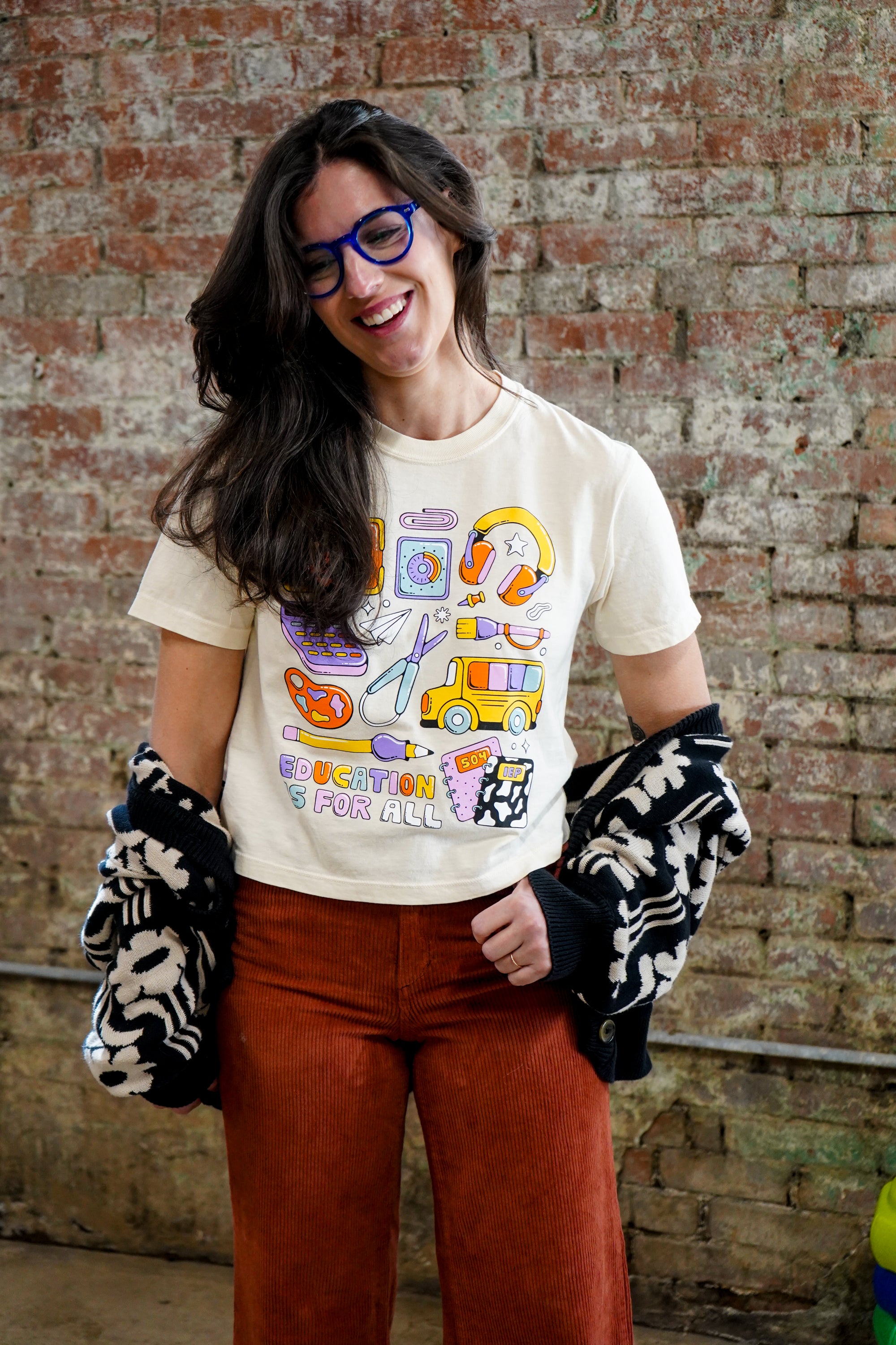 Woman wearing a graphic t-shirt and patterned gloves against a brick wall.