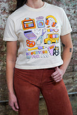 Person wearing a white t-shirt with colorful graphics and 'Education is for All' text against a brick wall.