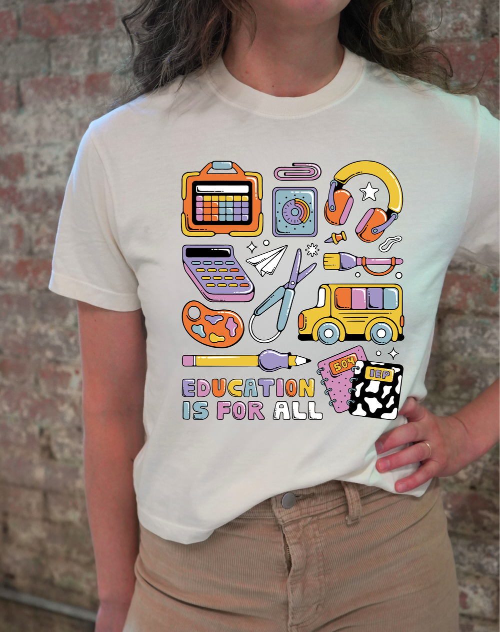Person wearing a white t-shirt with colorful graphic designs and 'Education is for All' text against a brick wall.