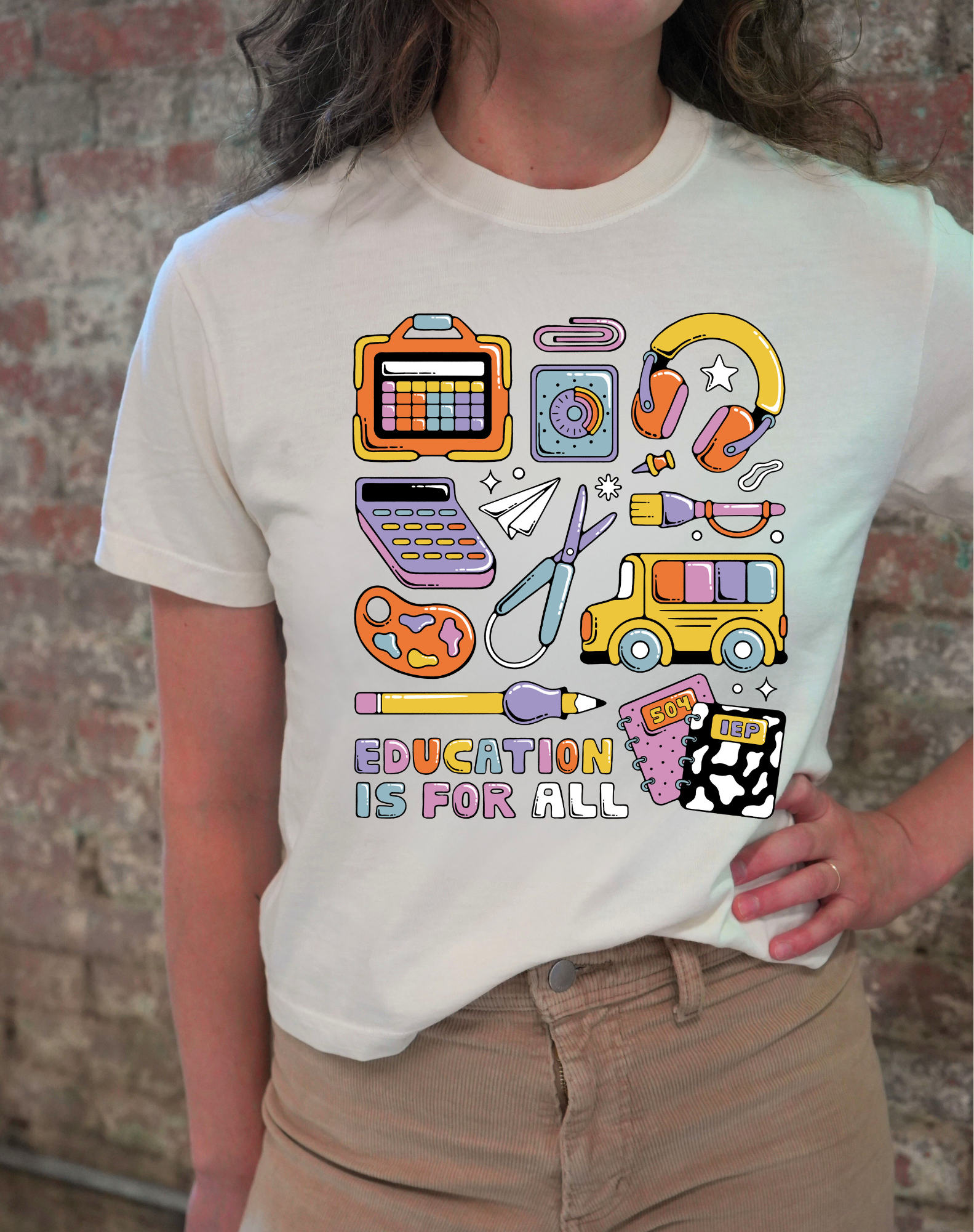 Person wearing a white t-shirt with colorful graphic designs and 'Education is for All' text against a brick wall.