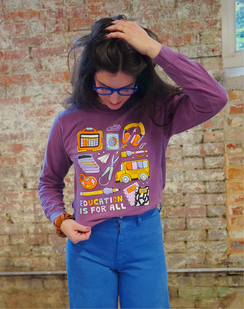 Person wearing a purple long-sleeve shirt with educational graphics and text, standing against a brick wall.