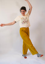 Person wearing a graphic t-shirt and mustard yellow pants on a white background