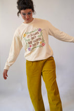 Person wearing a cream sweatshirt with text and graphics, standing against a plain background
