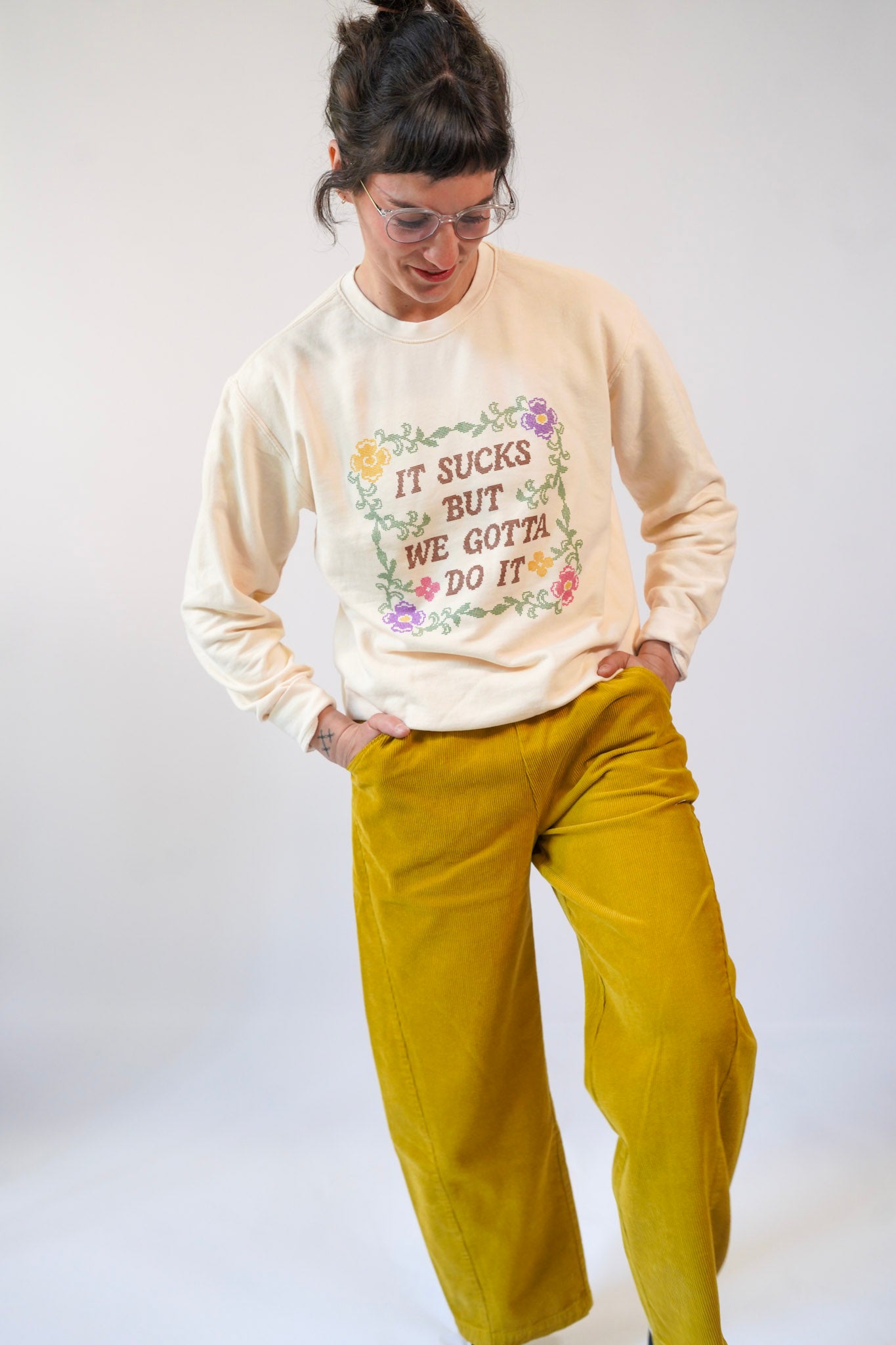 Person wearing a beige sweatshirt with floral text design and mustard yellow pants on a white background
