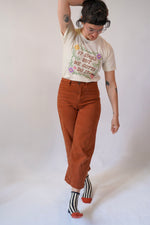 Person wearing a graphic t-shirt, brown pants, and striped socks on a white background