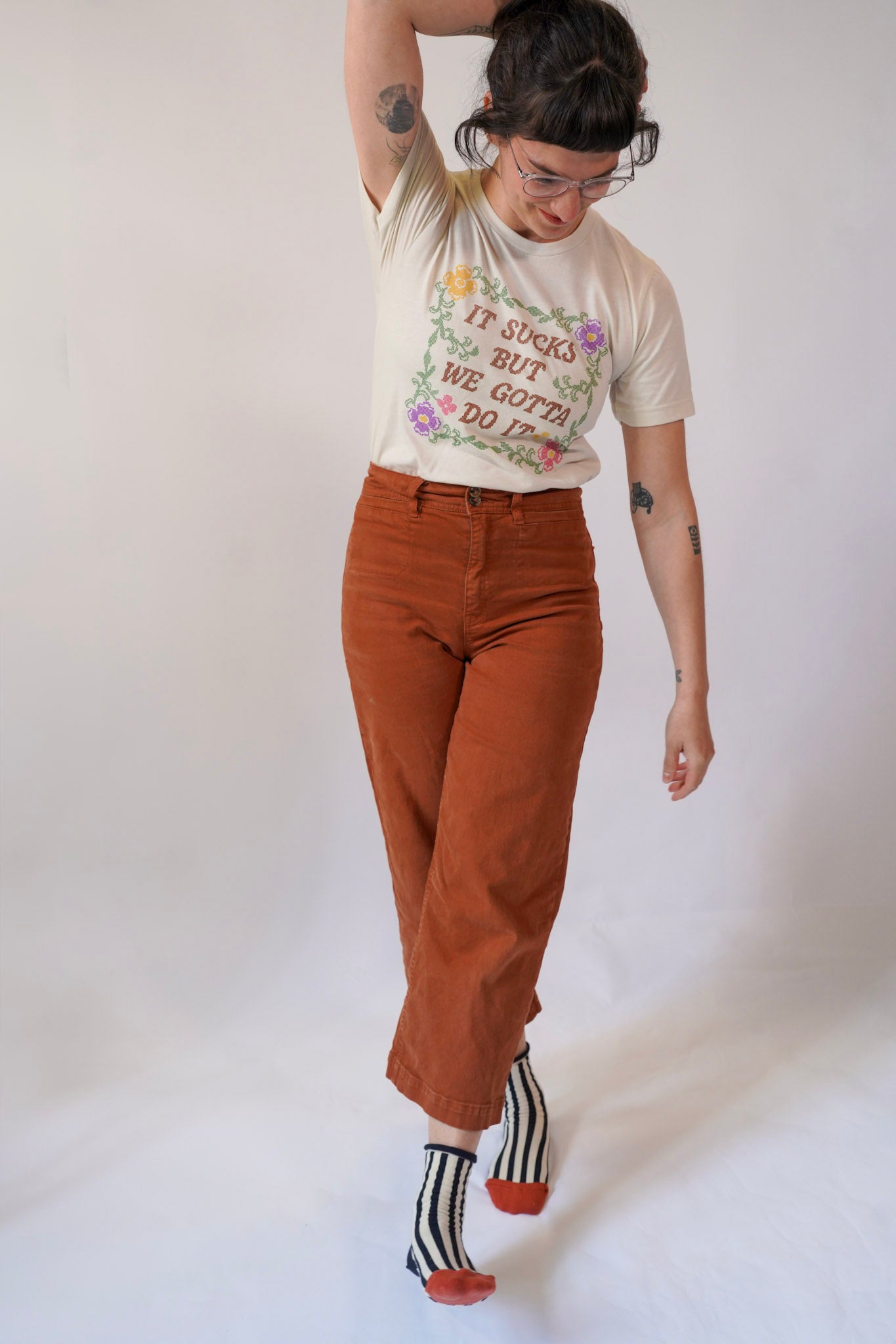 Person wearing a graphic t-shirt, brown pants, and striped socks on a white background