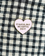 Heart-shaped enamel pin with text on a checkered fabric background
