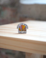 An enamel pin with the inscription 'MEET KIDS WHERE THEY ARE' in multicolored letters on a flat surface.